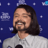 a man with long hair and a beard is smiling in front of a blue backdrop that says disney expo