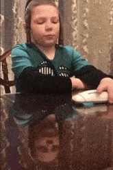 a young girl sitting at a table with a mouse