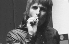 a black and white photo of a man in a leather jacket smoking a cigarette .