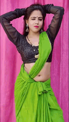 a woman in a green saree and a black blouse is posing for a picture .