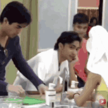 a group of people are gathered around a sink in a kitchen and one of them is wearing a towel on her head