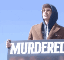 a man holding a sign that says murdered in white letters