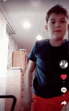 a boy in a blue shirt and red shorts is standing in a room with a heart on the bottom right