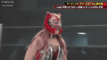 a female wrestler wearing a red mask stands in front of a sign that says stardom on it