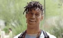 a young man with dreadlocks is smiling and wearing a camera strap around his neck .