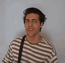a young man wearing a striped shirt and a black strap is smiling .