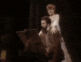 a man with a beard is sitting in front of an easel with a woman standing behind him adjusting his hair .