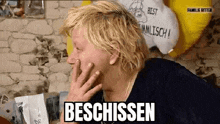 a man with blonde hair is covering his mouth with his hand and making a funny face .