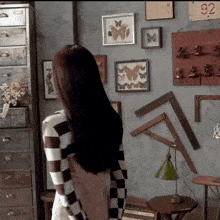 a woman in a checkered dress stands in front of a wall with framed butterflies on it