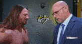 a man in a suit and tie talks to a shirtless wrestler
