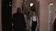 a group of people are walking down a hallway with a nbc logo in the background