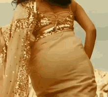 a woman in a gold sequined top and a gold saree is standing in the desert .