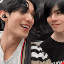 a man wearing ear buds is smiling next to another man wearing a black shirt that says why