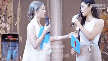 two women are standing next to each other holding microphones and a sign that says 7 on it .