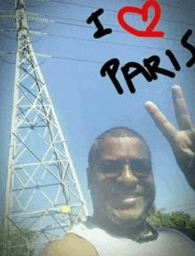 a man giving a peace sign in front of a tower that says i love paris on it