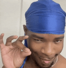 a man wearing a blue du rag is smiling and making a peace sign with his hand .