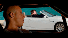 a man sitting in a car looking out the window at another man driving a white car