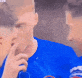 a man in a blue shirt is holding his finger to his mouth .