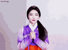 a woman wearing a purple and orange hanbok with her hands folded in front of her face .