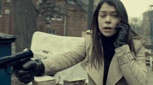 a woman is holding a gun and talking on a phone