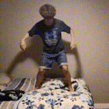 a young boy jumping on a bed with a floral blanket