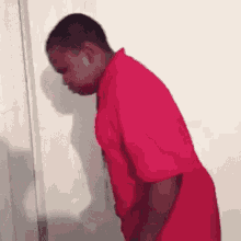 a man in a red shirt is standing in front of a white wall .