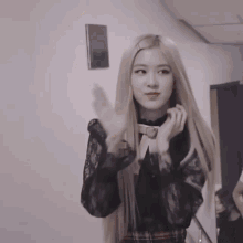 a woman with long blonde hair is standing in a room with her hands on her face .