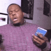 a man in a plaid shirt is holding a cell phone and making a funny face .