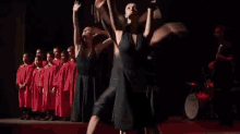 a man in a suit and tie stands in front of a microphone while two women dance around him