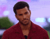 a man with a beard is wearing a red shirt and earrings and looking at the camera .