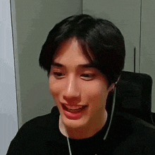 a young man wearing headphones and a black shirt is smiling while sitting in a chair .