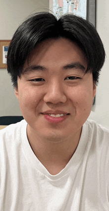 a young man wearing a white t-shirt smiles for the camera