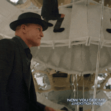 a man in a suit and hat stands in front of a mirror with the words now you see me