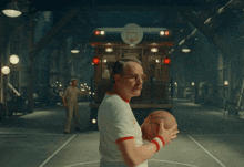 a man in a white shirt stands in front of a train with a basketball hoop on top of it