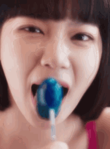 a woman is licking a blue lollipop in her mouth