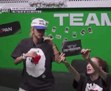 a man and a woman are standing in front of a green wall holding a sign that says ' tear ' .