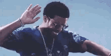 a man in a blue shirt and sunglasses is waving his hand in the air .
