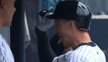 two baseball players are standing next to each other and one is wearing a black helmet .