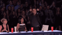 a man is sitting at a table with a microphone in front of a crowd of people applauding .