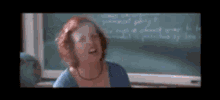 a woman is laughing in front of a chalkboard in a classroom