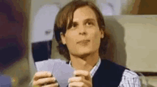 a man is holding two playing cards in his hands and looking at the camera .