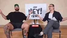 two men are sitting in front of a sign that says hey