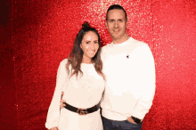 a man and a woman posing for a picture in front of a red background
