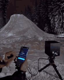 a person is using a cell phone in the snow while a large snowy hill is in the background