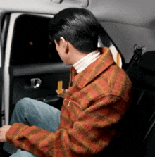 a man is sitting in the back seat of a car looking out the window .