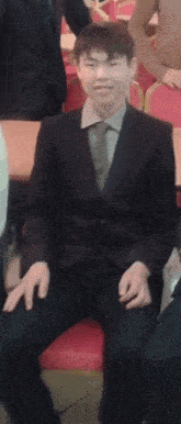a man in a suit and tie is sitting on a red chair and smiling .