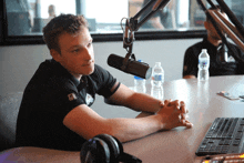 a man sits at a table in front of a microphone with his hands folded in front of him