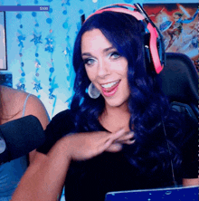 a woman with blue hair is smiling in front of a screen that says $ 100 on it