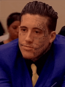 a man in a blue suit and tie has a tattoo on his face that says " why "