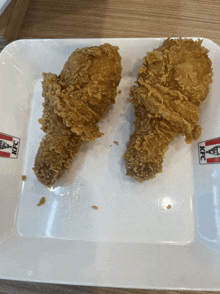 two fried chicken legs on a white plate with a kfc logo on it